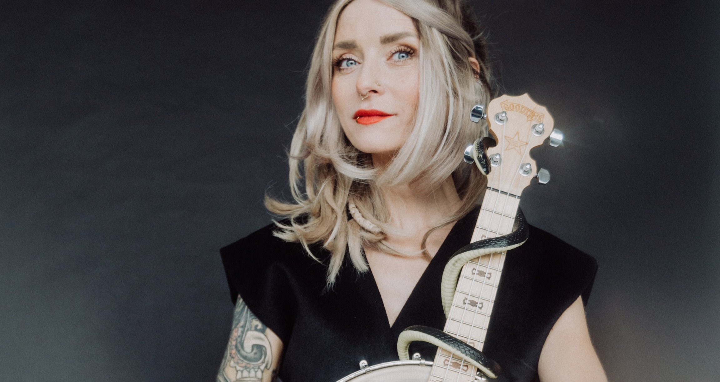 Foto der Künstlerin mit einem Instrument in den Händen vor grauem Hintergrund.