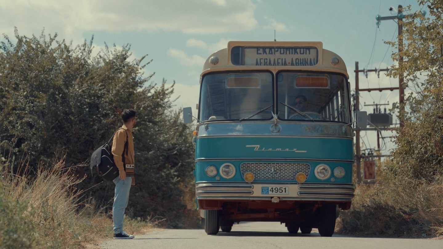 Ein Foto für das Event „KURZFILME AUS GRIECHENLAND“ bei der Griechischen Filmwoche München: Ein Mann wartet auf einen blauen Bus.