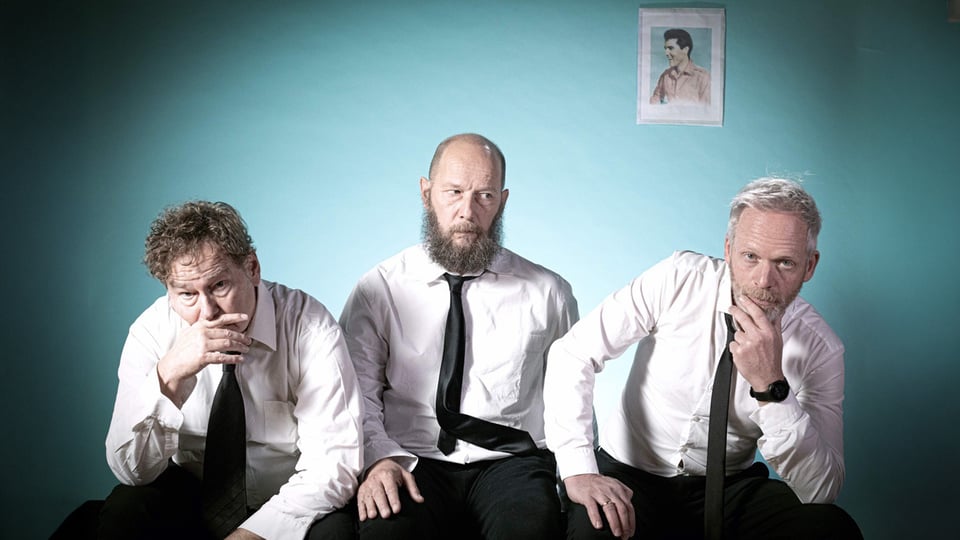 Die drei Bandmitgllieder in weißen Hemden vor blauem Hintergrund