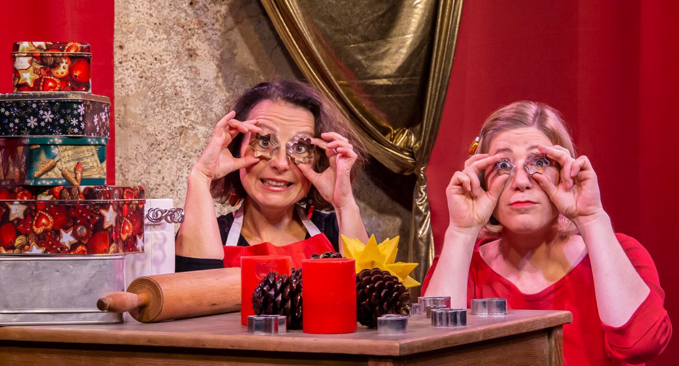 Zwei Damen mit Plätzchenausstechern vor die Augen haltend in weihnachtlichem Ambiente an Tisch sitzend 