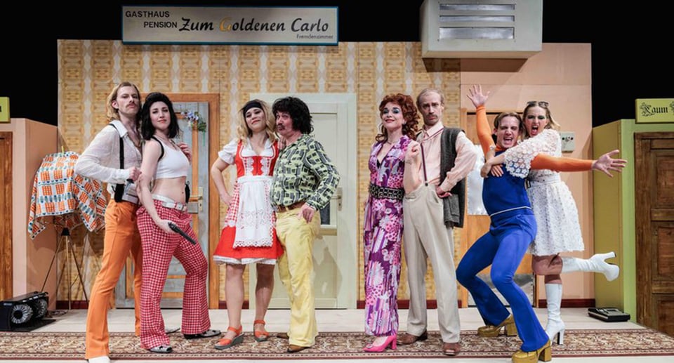acht Personen in bunter Kleidung auf Theaterbühne