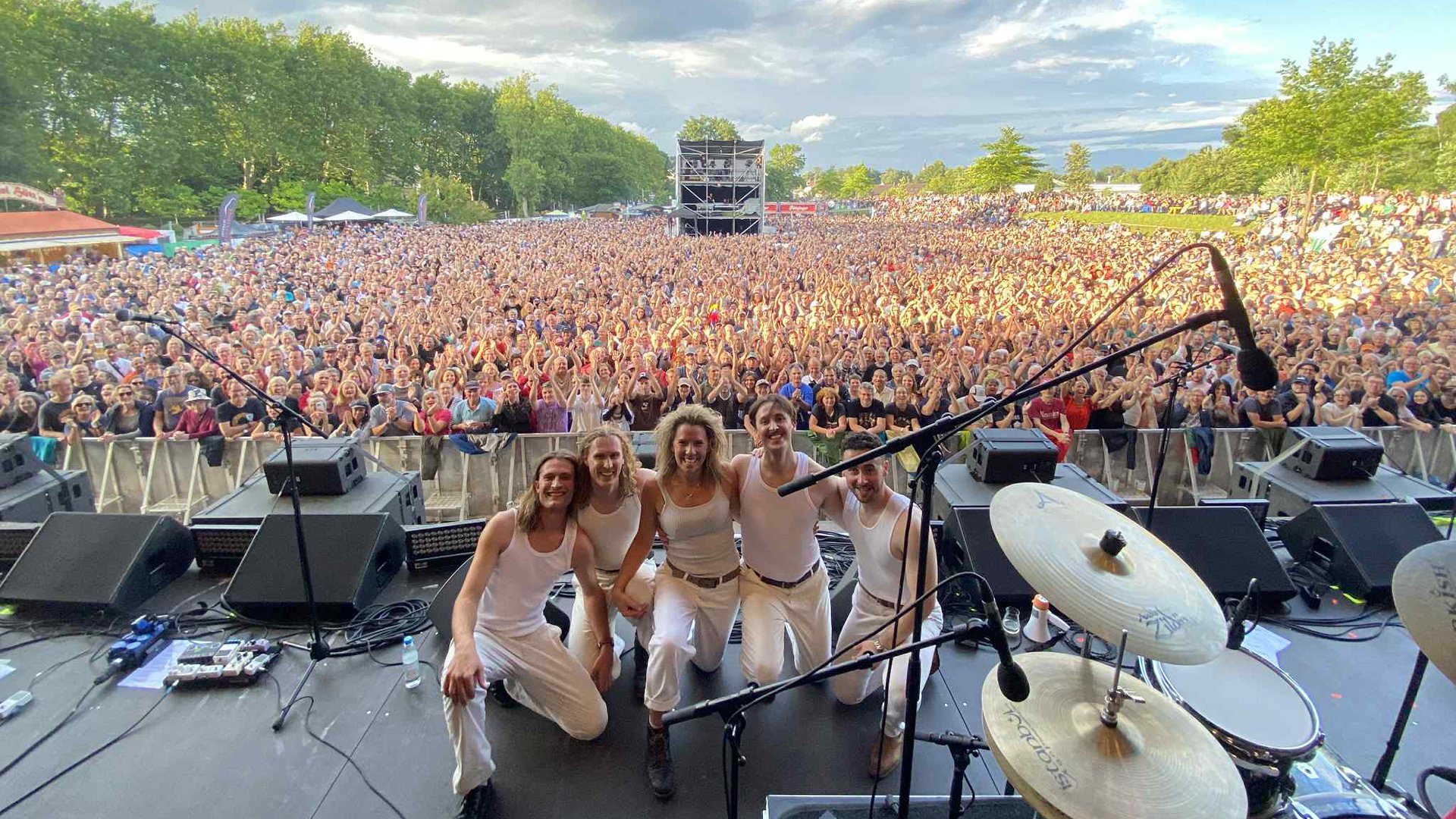 Bild der Band in weißer Kleidung auf einer Open Air Bphne, im Hintergrund Publikum