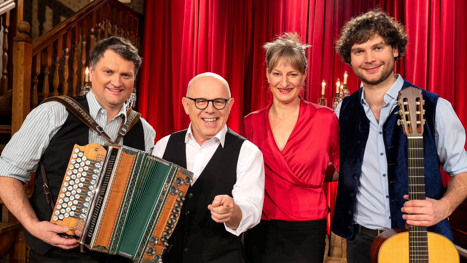 Foto für die Veranstaltung von Die Couplet-AG mit der Gruppe, einigen Instrumenten und roten Vorhängen im Hintergrund