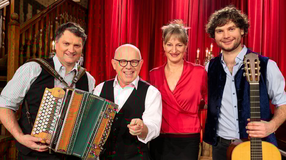 Foto für die Veranstaltung von Die Couplet-AG mit der Gruppe, einigen Instrumenten und roten Vorhängen im Hintergrund