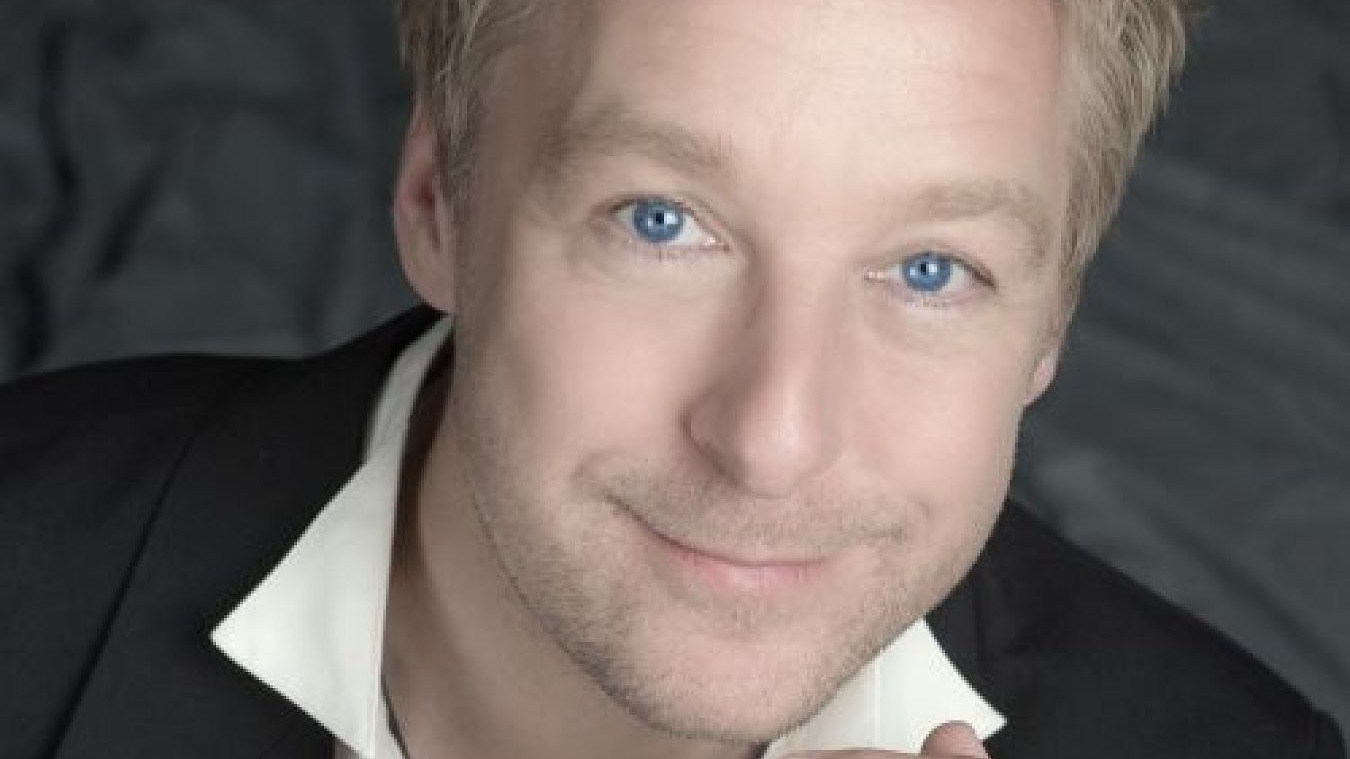 Portrait einer Person mit schwarzem Sakko undweißem Hemdkragen vor grauem Hintergrund