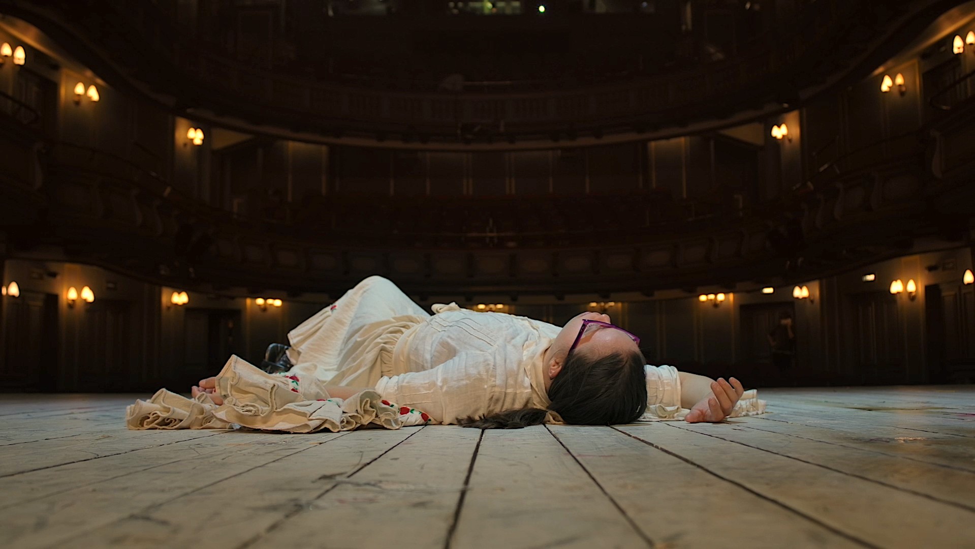 Ein Foto für das Event „LOXY“ bei der Griechischen Filmwoche München: Eine Person liegt auf dem Boden und trägt weiße Kleidung.