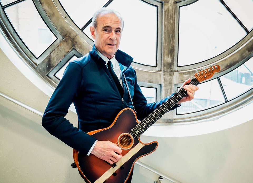 Ein Mann mit einer Gitarre und einer runden Fenster im Hintergrund