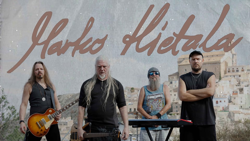 Eventfoto für „MARKO HIETALA“ mit den Künstlern mit Instrumenten vor dem Hintergrund eines Dorfes.