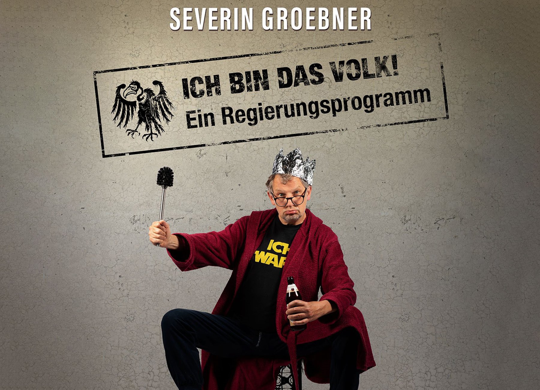 Mann mit Krone  n rotem Bademantel  und Toilettenbürste in der Hand sowie Aufschrift