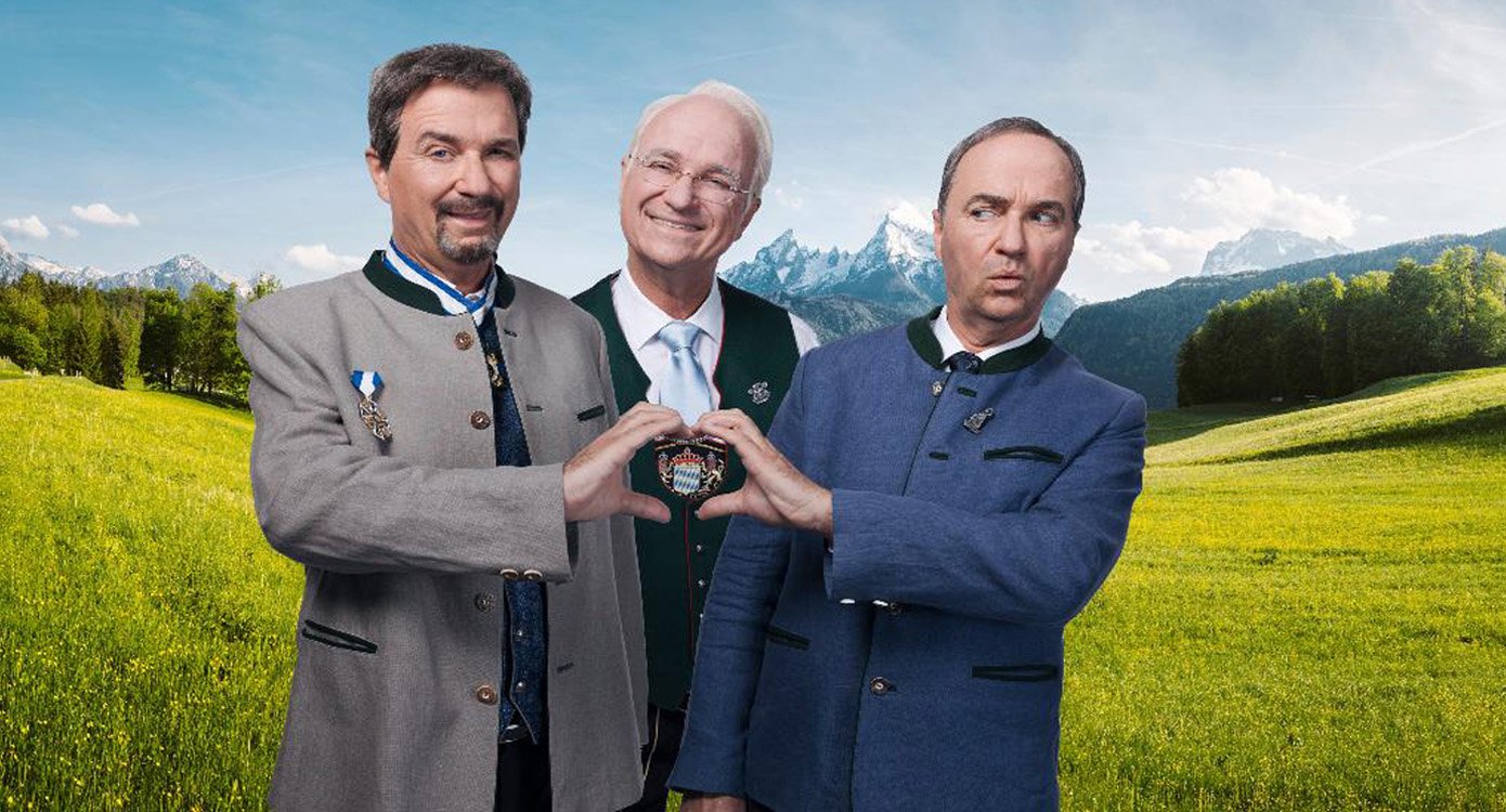 Eine Collage aus drei Fotos, mit Wolfgang Krebs und zwei Darstellern von Markus Söder und edmund Stoiber auf einer Wiese mit Bergen im Hintergrund