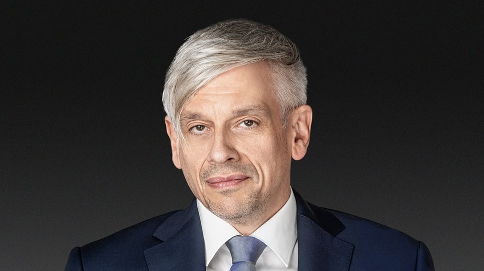 Mathias Tretter in dunkelblauem Anzug mit weißem Hemd vor dunkelgrauem Hintergrund