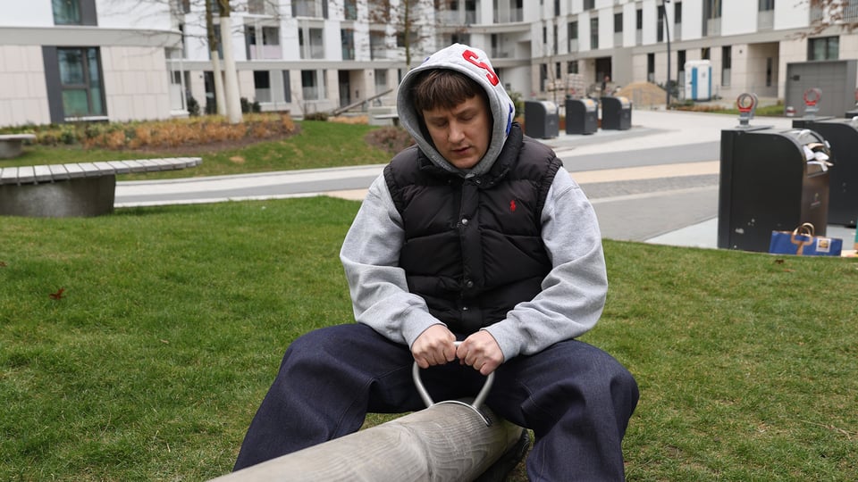Ein Mann mit Anorak und Kapoze sitz auf einer Wippe