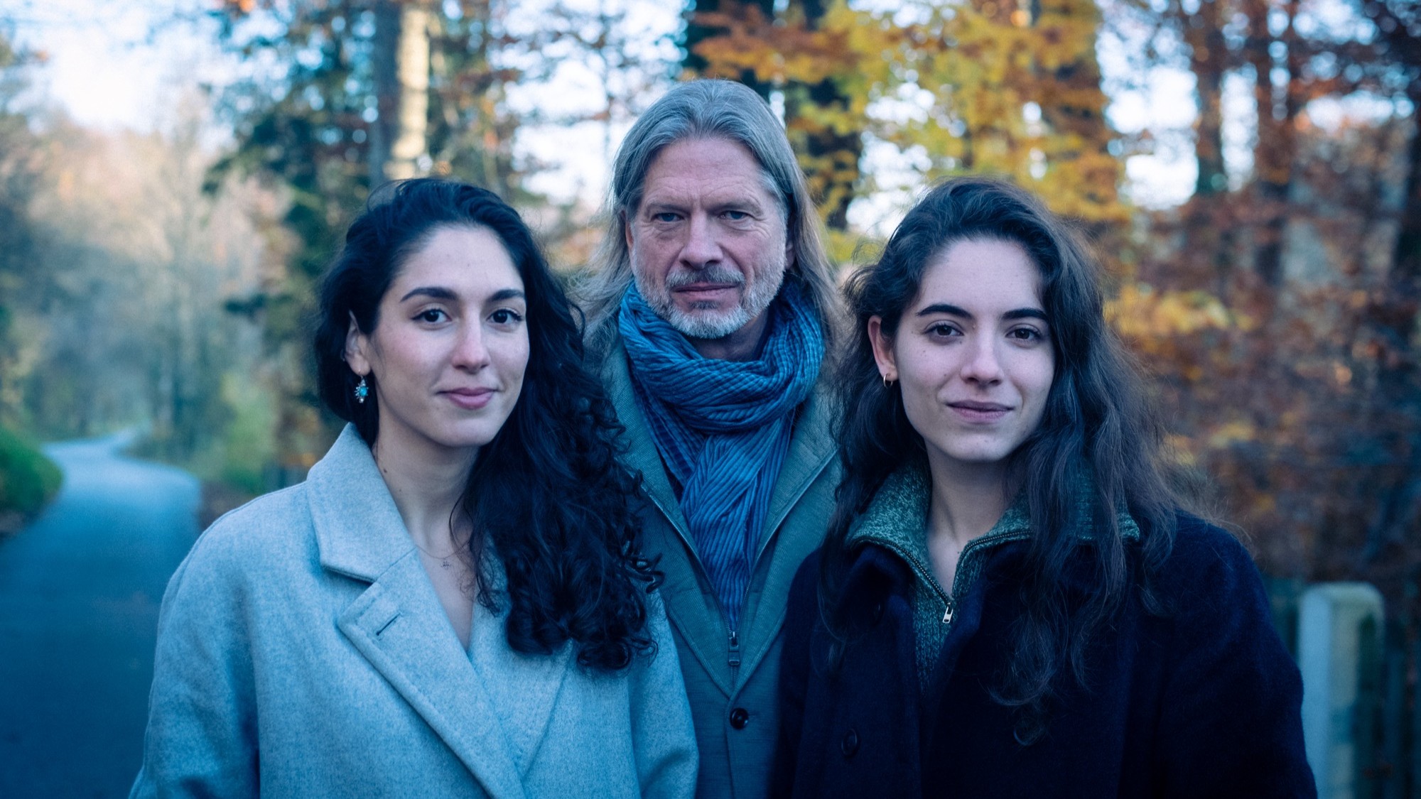 Das Ensemble Phoenix Munich mit drei Personen in Herbstkleidung auf einem Waldweg, vor herbstlich gefärbten Bäumen und unscharfem Hintergrund.
