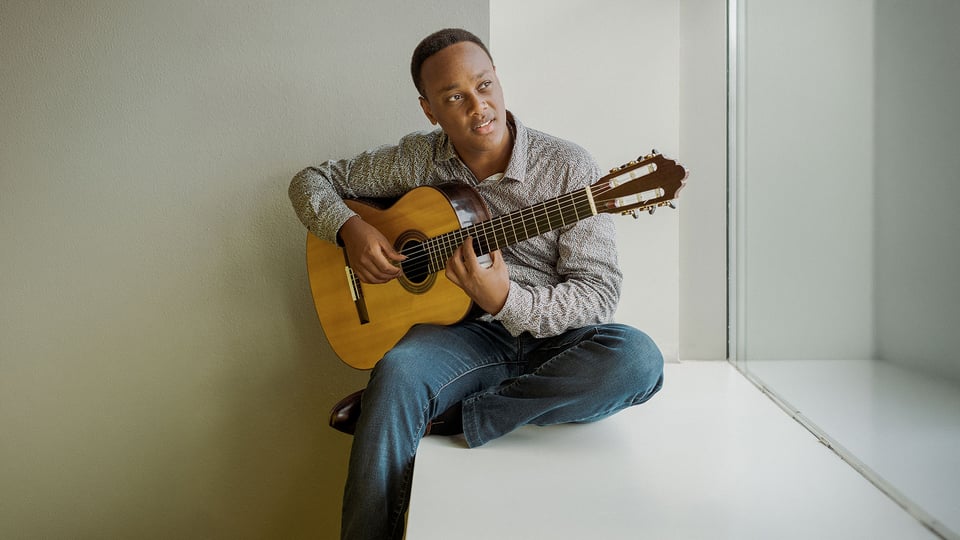 Der Gitarrist Raphaël Feuillâtre in Jeans und Freizeithemd auf einer Fensterbank sitzend mit Gitarre