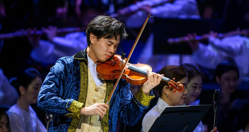 Mann auf Bühne mit Violine mit Orchester im Hintergrund