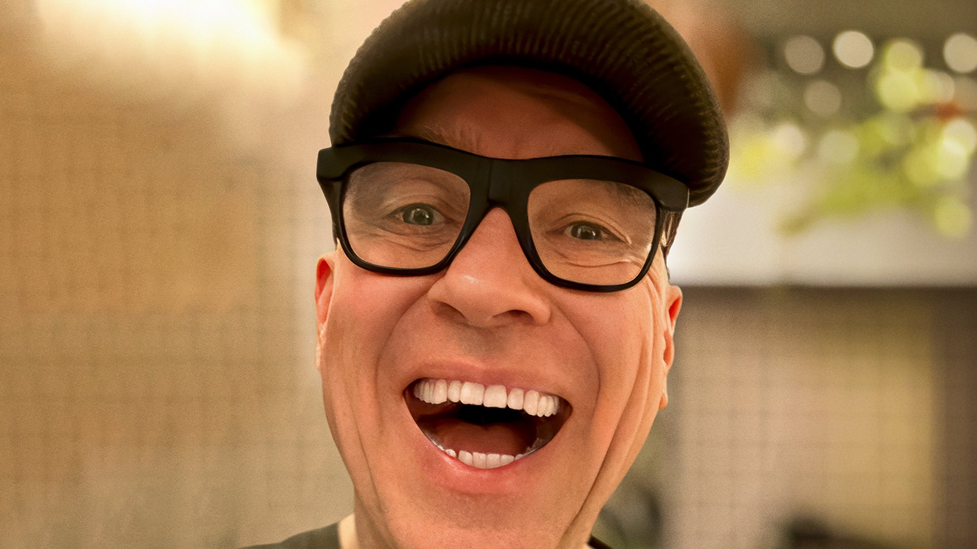 Der Künstler HG Butzko mit Brille und Kappe lacht in die Kamera