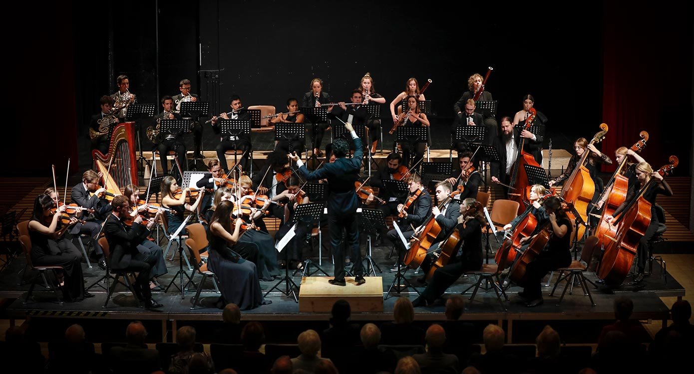 Foto eines Orchesters mit Instrumenten vor schwarzem Hintergrund.