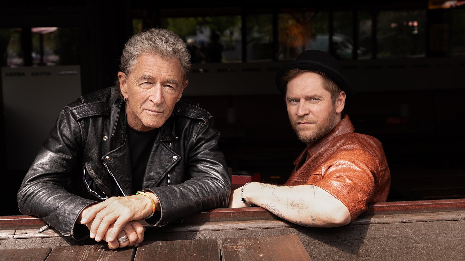 Musikerporträt von Peter Maffay und Johannes Oerding an einem Holztisch im Außenbereich, Lederjacken und urbanes Setting mit natürlichem Licht