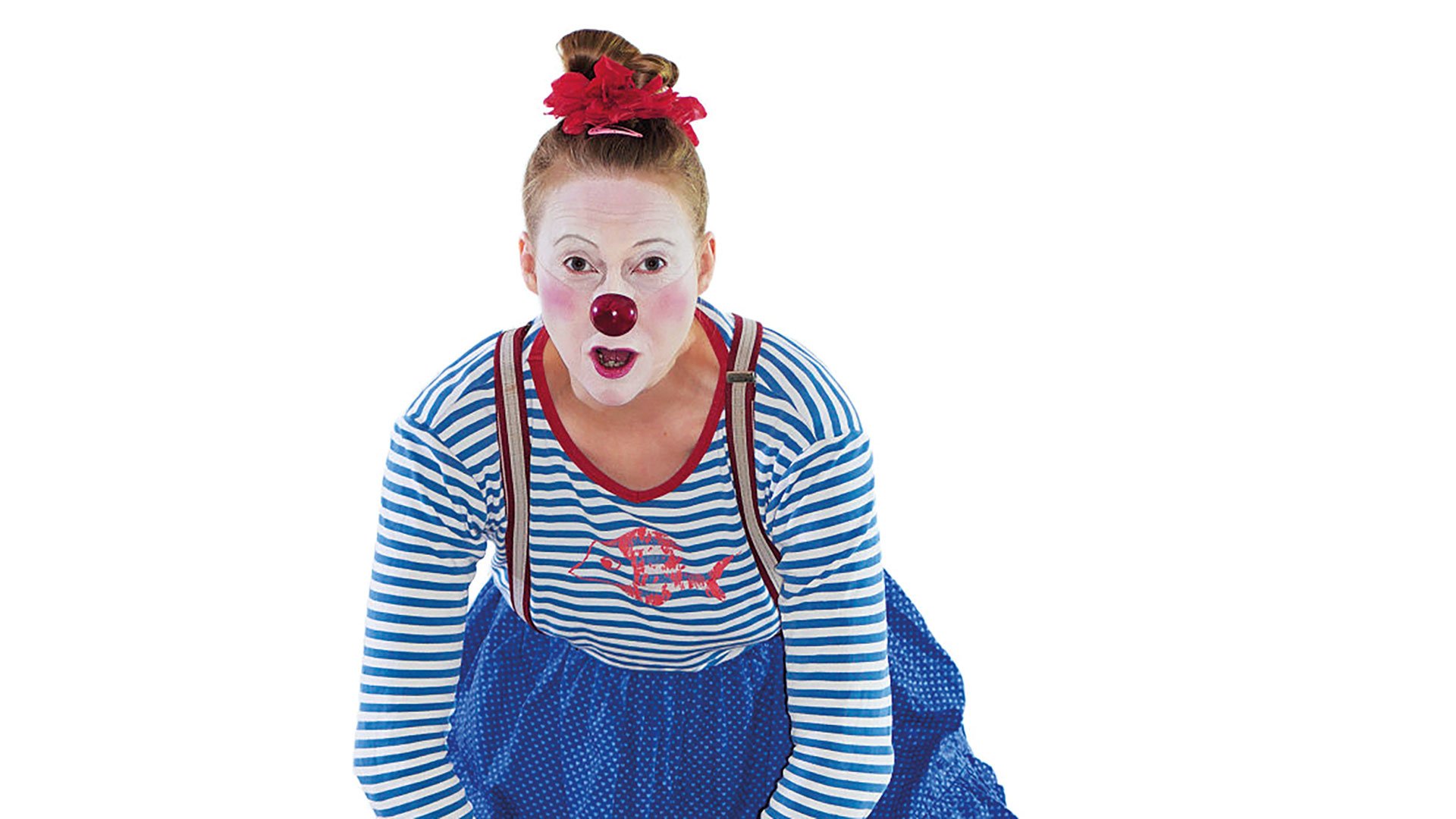 Porträtfoto mit Clownfigur mit weiß geschminktem Gesicht, roter Nase und blau weiß gestreiftem Oberteil, die sich nach vorne beugt, vor hellem neutralem Hintergrund