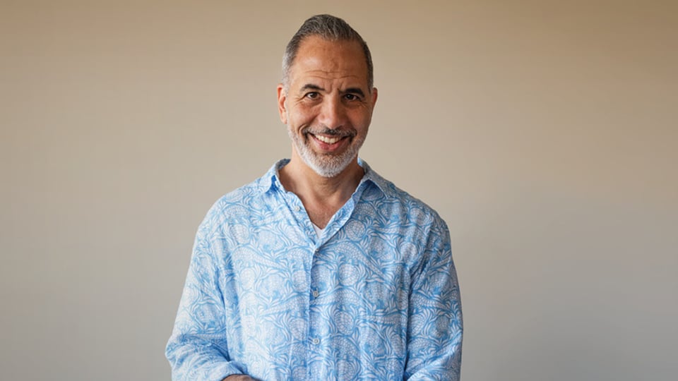 Porträtfoto für das Event von Yotam Ottolenghi: Eine einzelne Person steht vor neutralem, hellem Hintergrund und trägt ein hellblaues, gemustertes Hemd. Die Aufnahme ist frontal, gut ausgeleuchtet und ohne weitere Objekte oder Text im Bild.