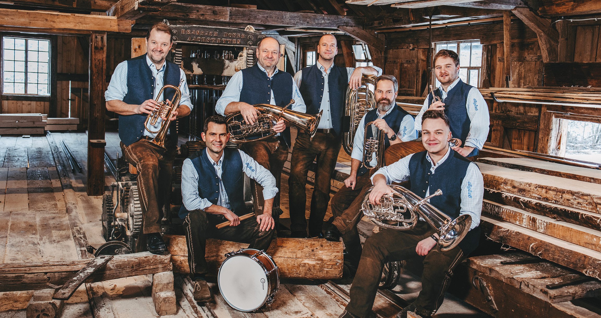 Foto der Gruppe mit Instrumenten und in bayerischer Tracht in einem holzvertäfelten Raum.