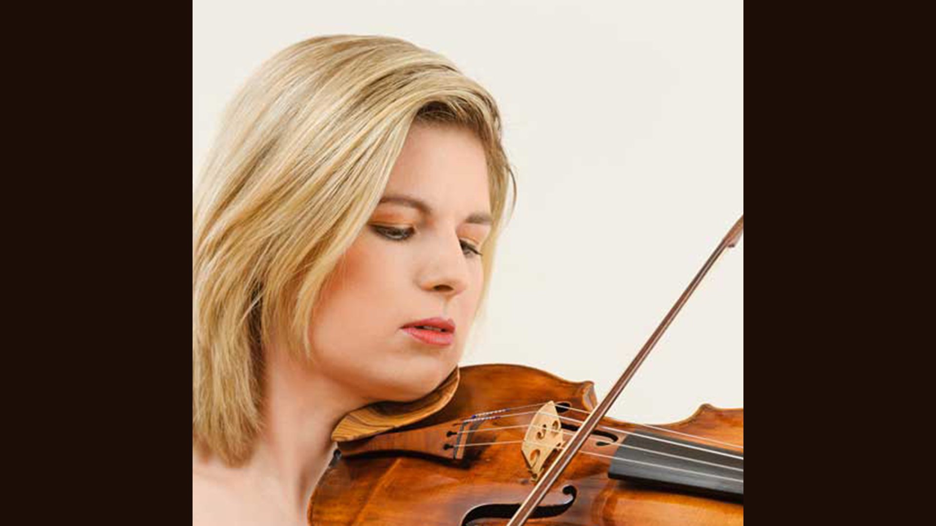 Porträtaufnahme von Cornelia Lö­scher mit hellblondem, schulterlangem Haar, die eine Geige hält; der helle Hintergrund lässt die warmen Holztöne des Instruments deutlich hervortreten.