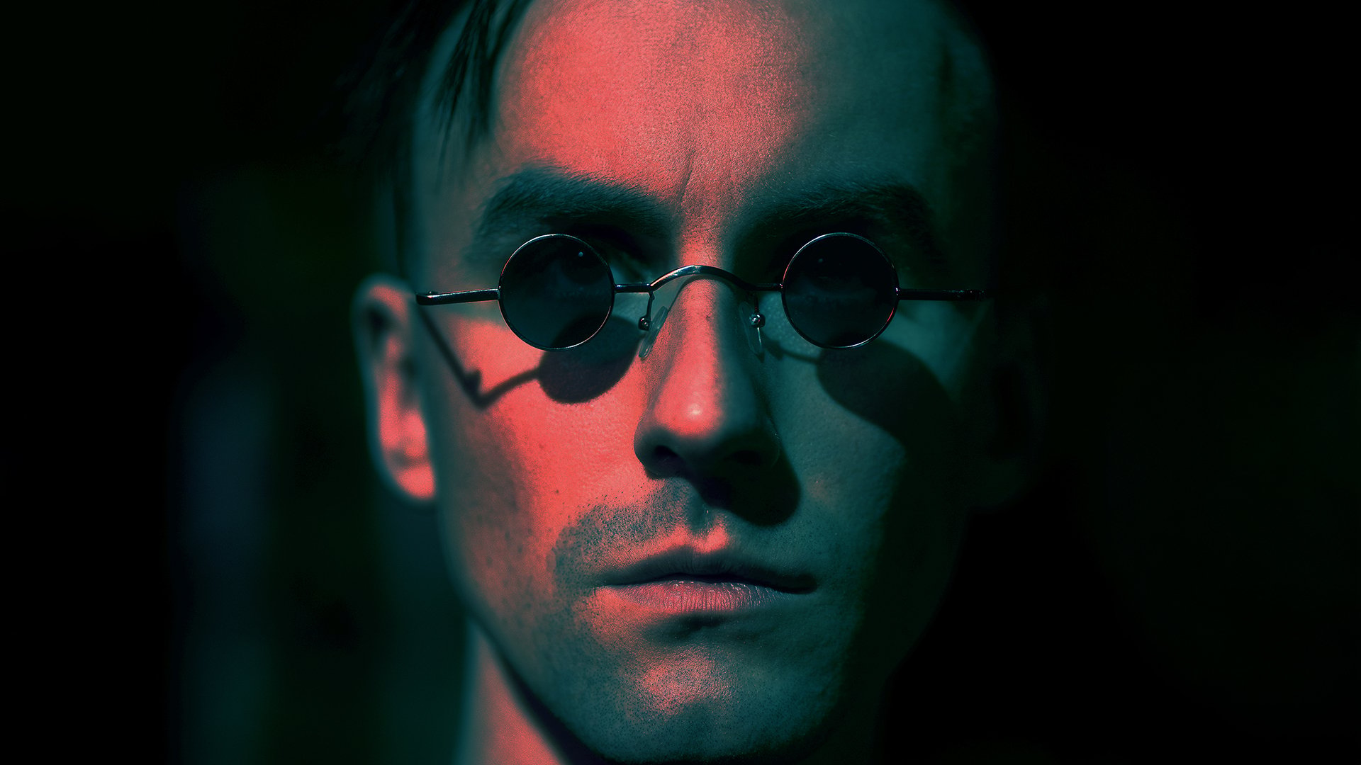 Portrait des Künstlers Venjent mit kleiner runder Sonnenbrille in rot-türkisem Licht mit starken Kontrasten