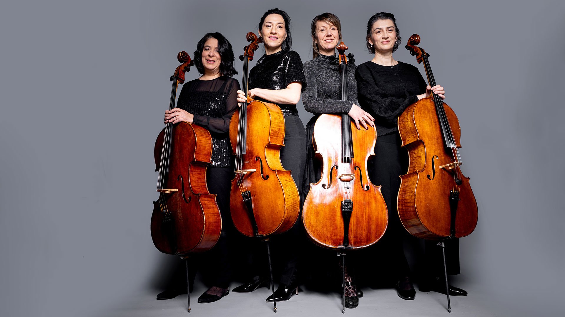 Classic Meets Pop Vol.2: Vier Musikerinnen mit Violoncelli stehen nebeneinander vor grauem Hintergrund und halten ihre Instrumente in den Händen.