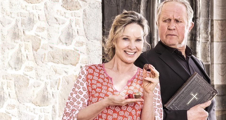 Ein Mann und eine Frau vor Steinmauer, sie mit rotem Kleid Schokoladekugeln in der Hand