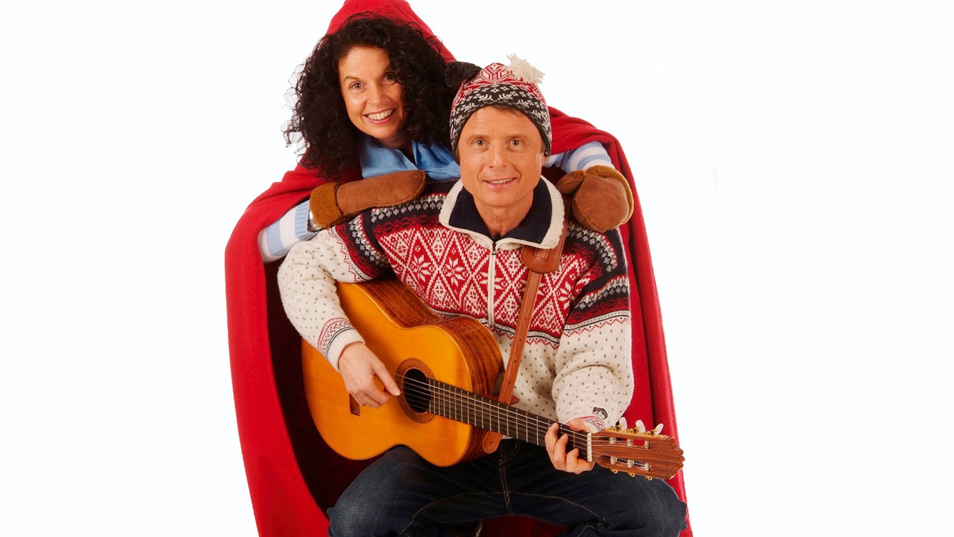 Pressefoto von Sternschnuppe mit zwei Personen in winterlicher Kleidung, eine Person mit Akustikgitarre in norwegischem Strickpullover und Mütze, die andere mit rotem Umhang und Fäustlingen, vor hellem Hintergrund
