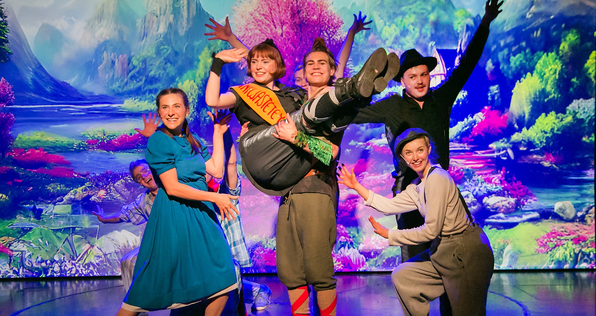 ein Bild des Musicals mit einigen der Darsteller vor einem farbenfrohen Hintergrund