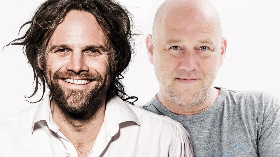 Zwei Männer (Keller Steff und Michi Dietmayr) in einem hellen Studio-Porträt, frontal blickend; links mit langen Haaren und Bart, rechts mit Glatze und grauem T-Shirt.