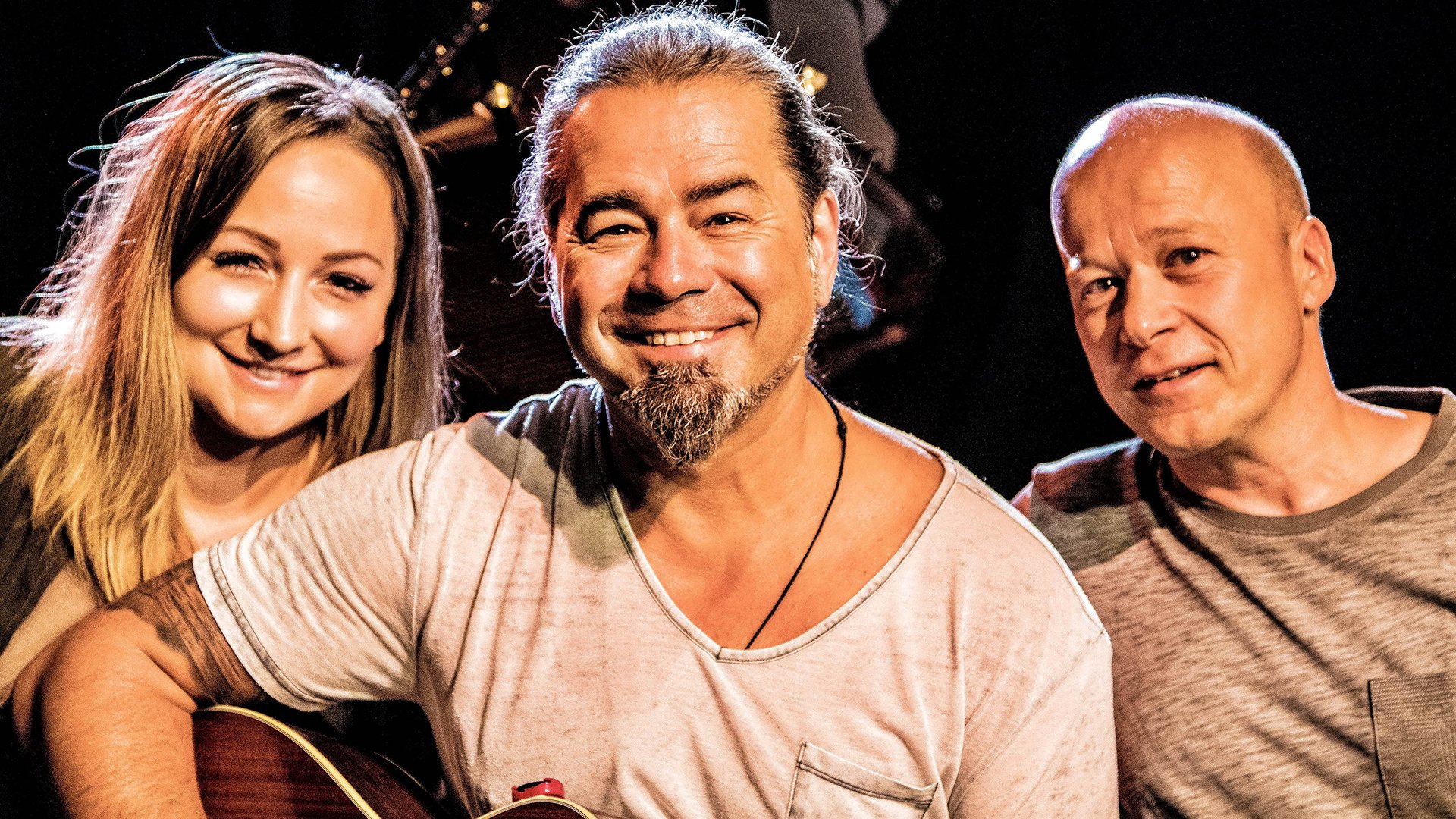 Eine Dame und zwei Herren, einer davon mit einer Gitarre in der Hand
