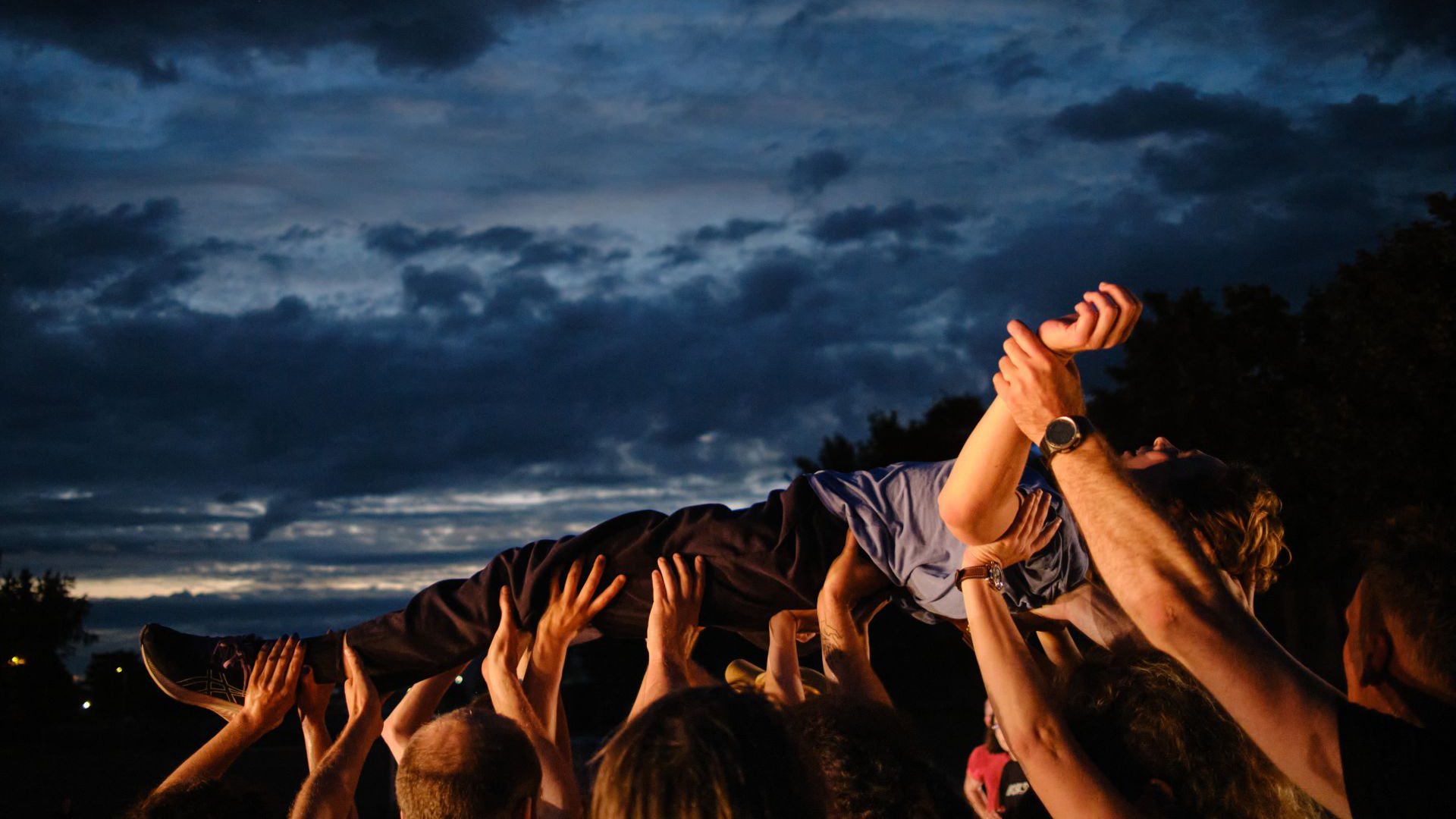 Eine Person wird im Freien von vielen erhobenen Händen über die Menge getragen, vor dunklem Abendhimmel.