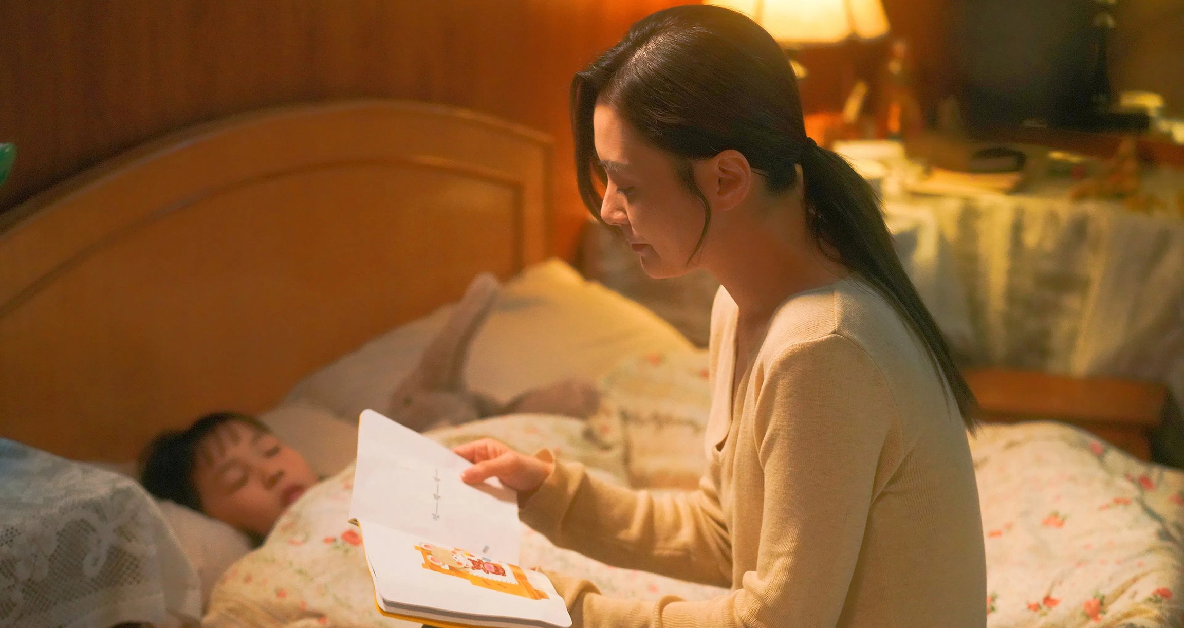 Eine Dame sitzt am Bett eines Kindes und liest aus einem Kinderbuch vor