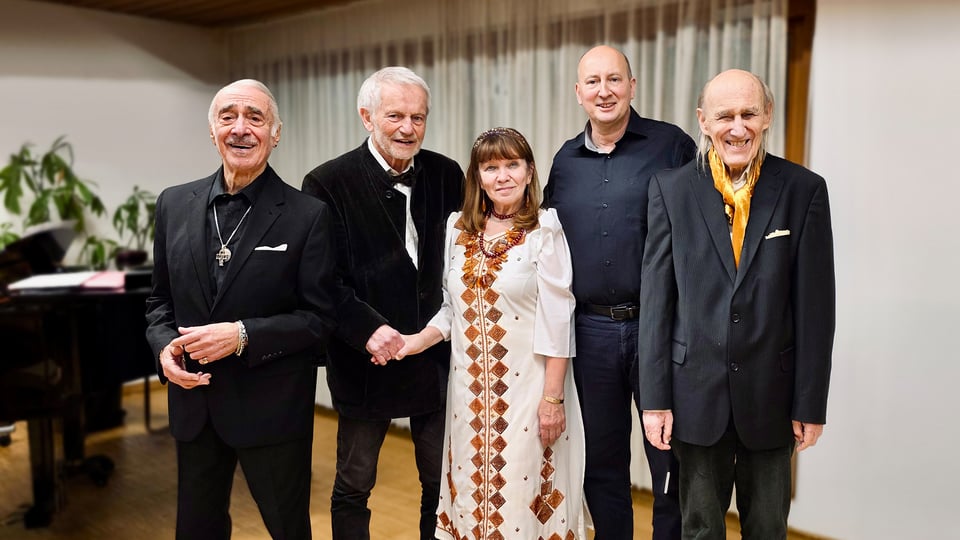Bildmotiv zum Event „Klang des Frühlings – Lieder mit Geschichte“: Gruppenfoto von fünf auftretenden Personen in einem Innenraum mit Holzboden und hellem Hintergrund. Die Gruppe steht nebeneinander vor einem geschlossenen Vorhang, im Hintergrund ist ein Klavier zu sehen. Die Szene vermittelt den Eindruck eines musikalischen Abends mit Gesang und Live‑Begleitung.