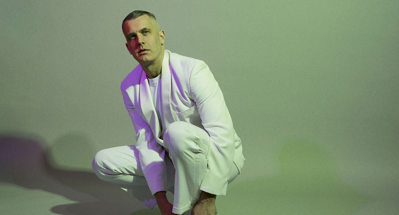 Ein Foto des Künstlers im weißen Anzug vor grünem Hintergrund