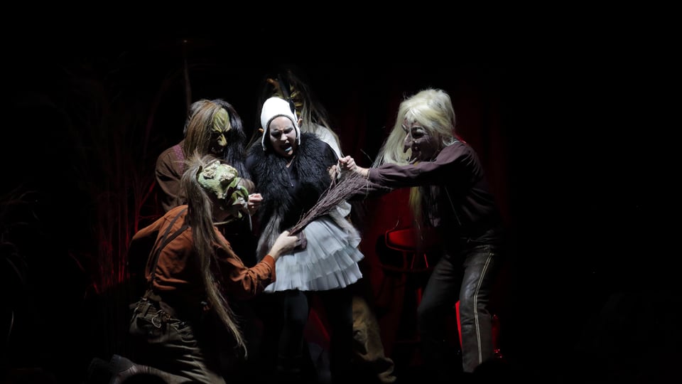 Vier maskierte Darsteller auf der Bühne in dunklem Licht