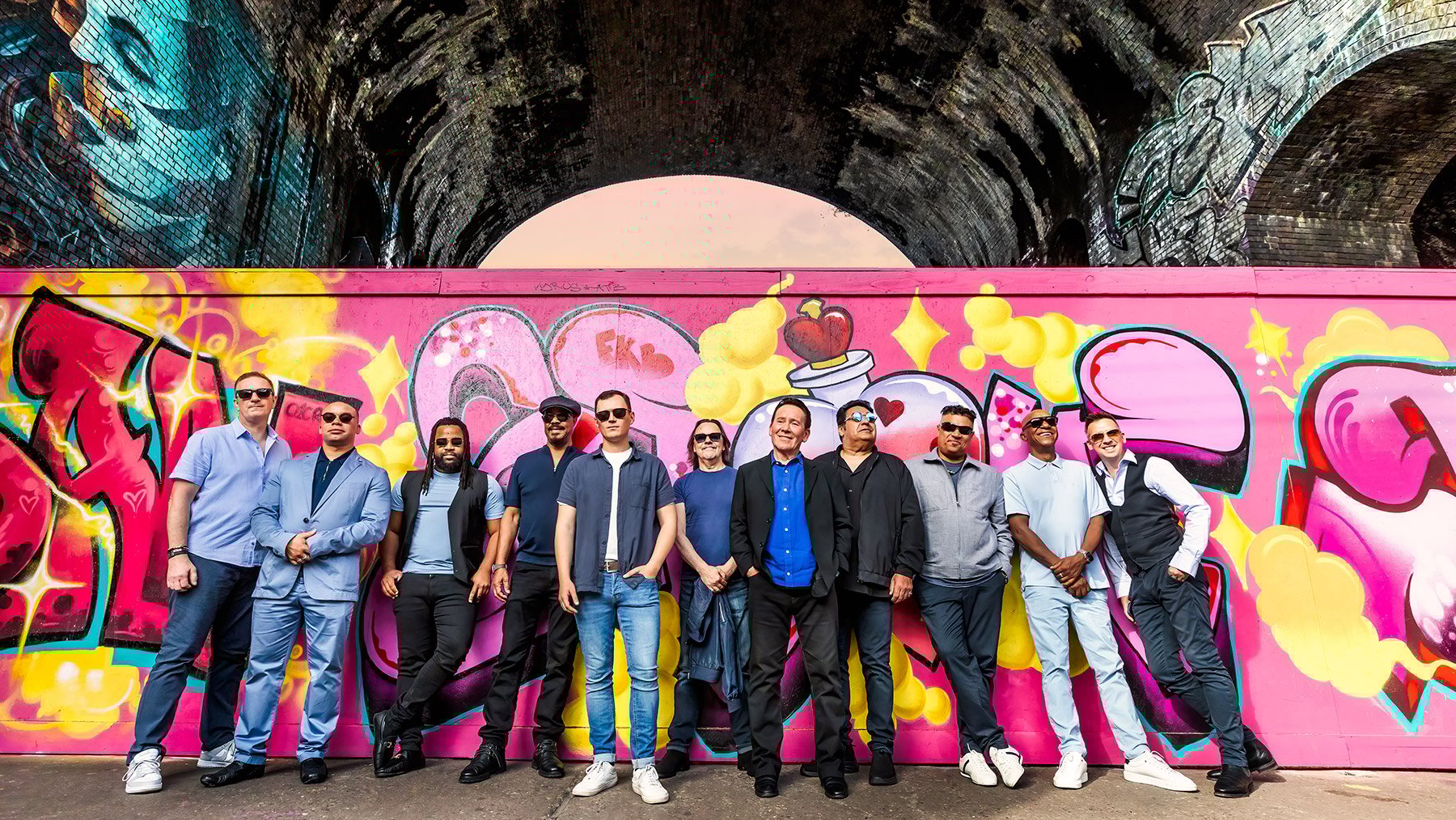 UB40 vor einer Wand mit Graffiti – Gruppenfoto der Band beim Event.
