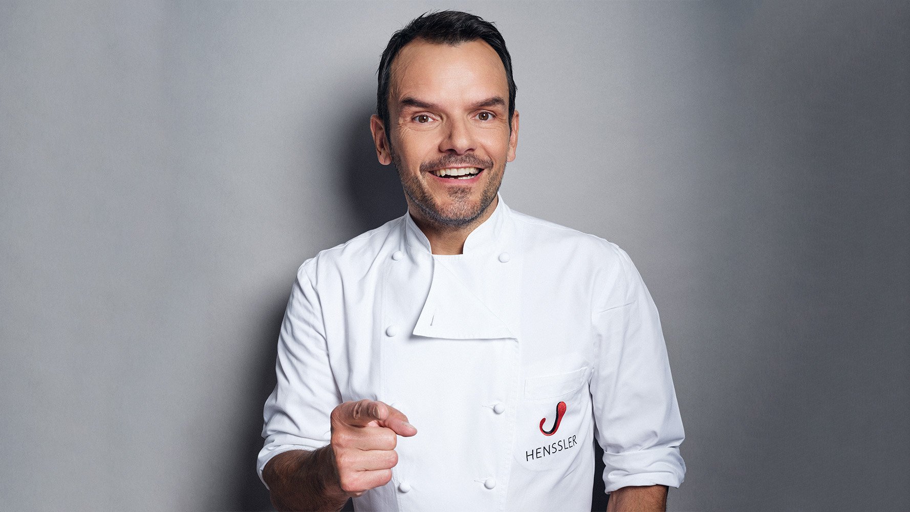 Auf dem Bild ist Steffen Henssler vor einem grauen Hintergrund zu sehen