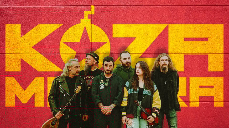 Sechs Personen stehen vor einer rot-gelben Wand mit großem ‚KOZA MOSTRA‘‑Schriftzug; einige halten Musikinstrumente wie Bouzouki und Geige, alle tragen legere bis rockige Kleidung