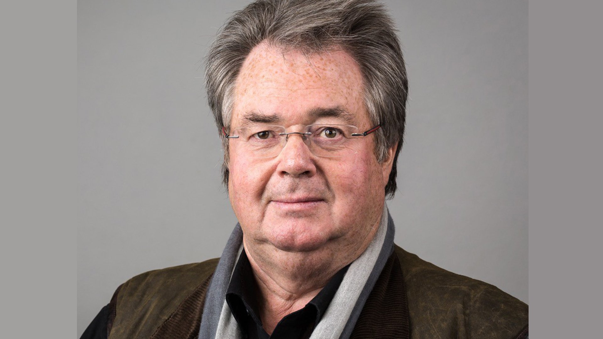 Ein Portrait des Künstlers Enjott Schneider vor grauem Hintergrund