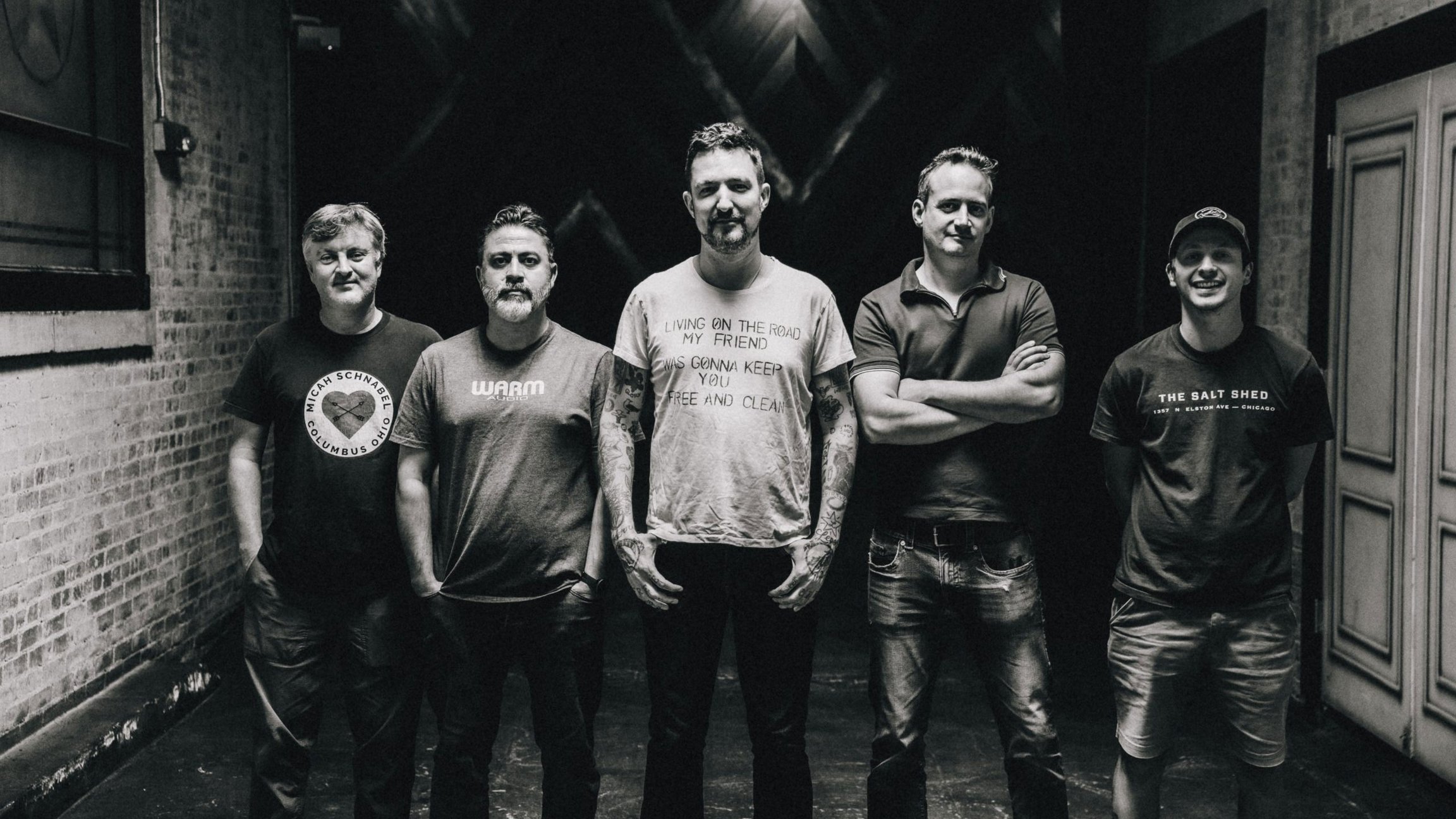 Fünf Bandmitglieder der Frank Turner & The Sleeping Souls stehen in einem schwarzweißen Backsteingang unter dramatischer Beleuchtung, das mittlere trägt ein helles T-Shirt mit Schriftzug