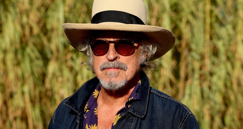 Foto des Künstlers BAP mit Hut, Sonnenbrille und Jeansjacke vor unscharfem Hintergrund.