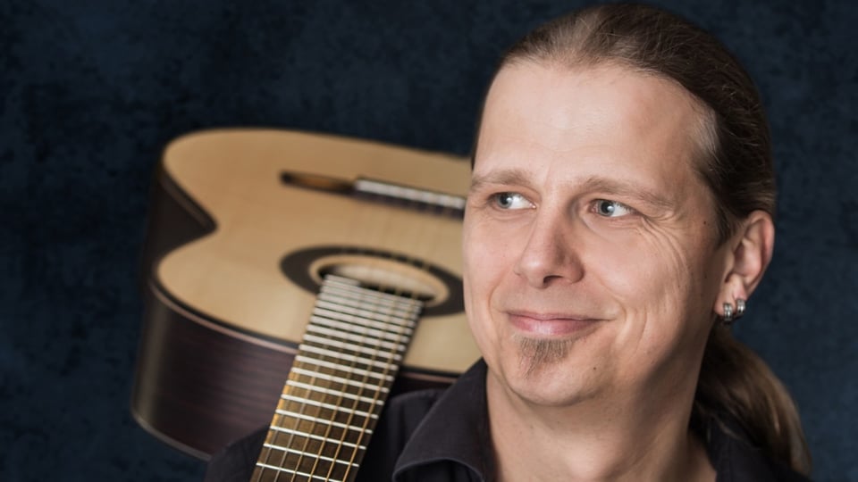 Ein Portrait von Stefan Eichner mit einer Akustikgitarre im Hintergrund
