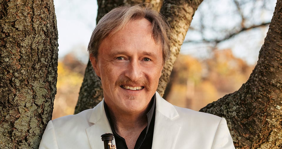 Portrait von blondem Mann mit weissem Sakko vor Baumstämmen