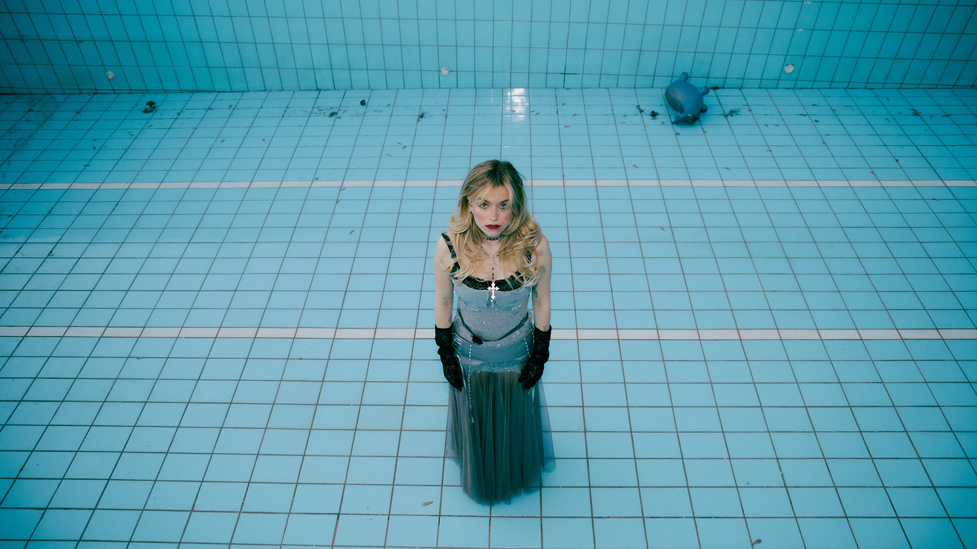 Ene blonde Dame in blauem Kleid steht in einem blau gefliesten Becken