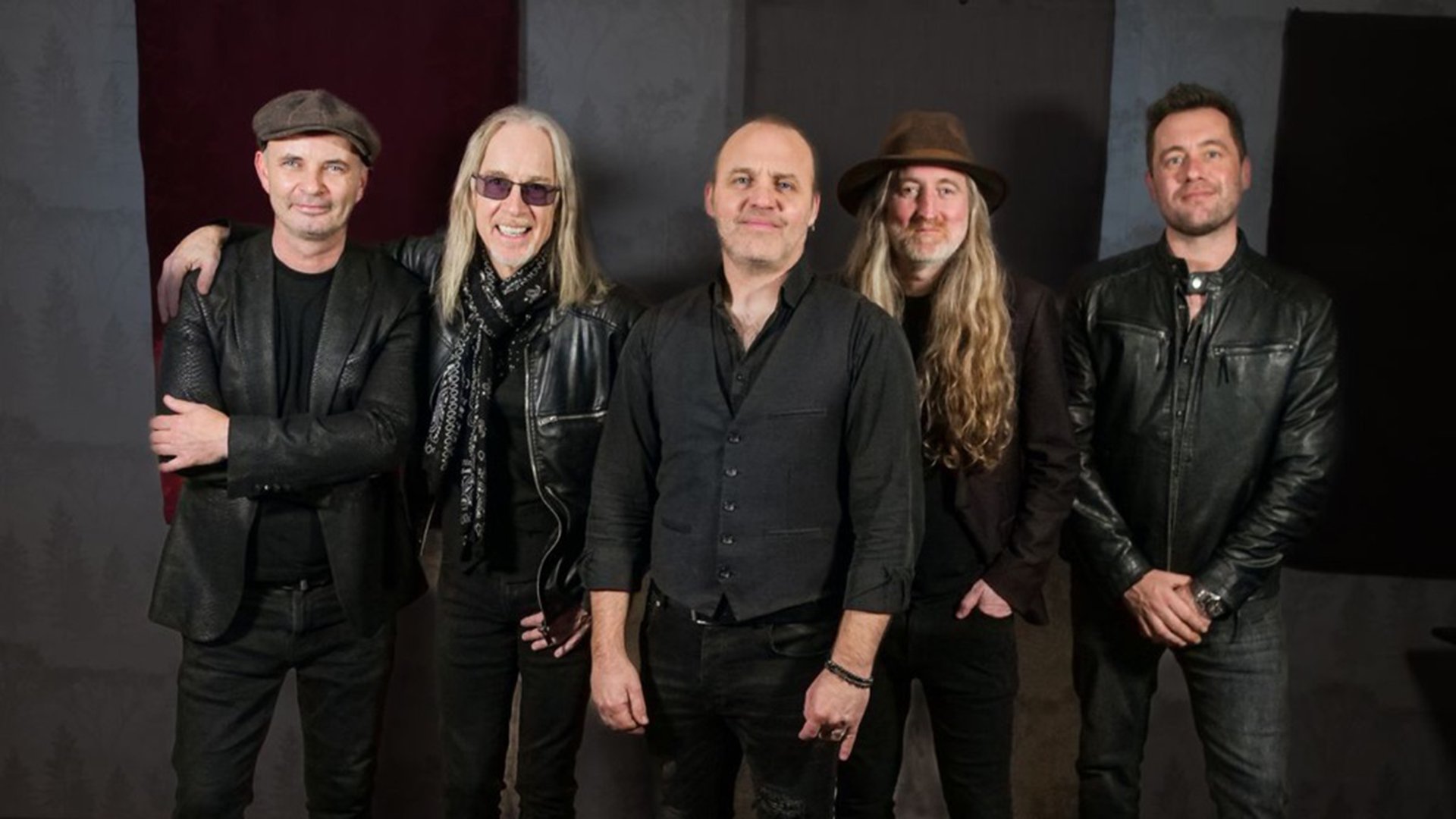 Fünf Musiker der Band vor einem gestreiften Hintergrund