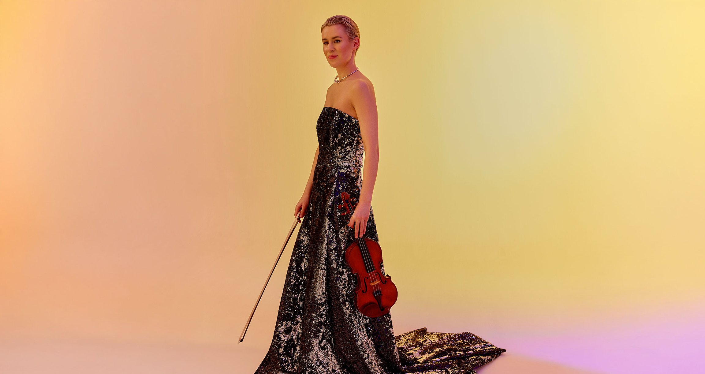 Eine Frau in einem langen, sehr eleganten Kleid mit einem Instrument in der Hand, vor einem Hintergrund in Gelb, Rosa und Orange
