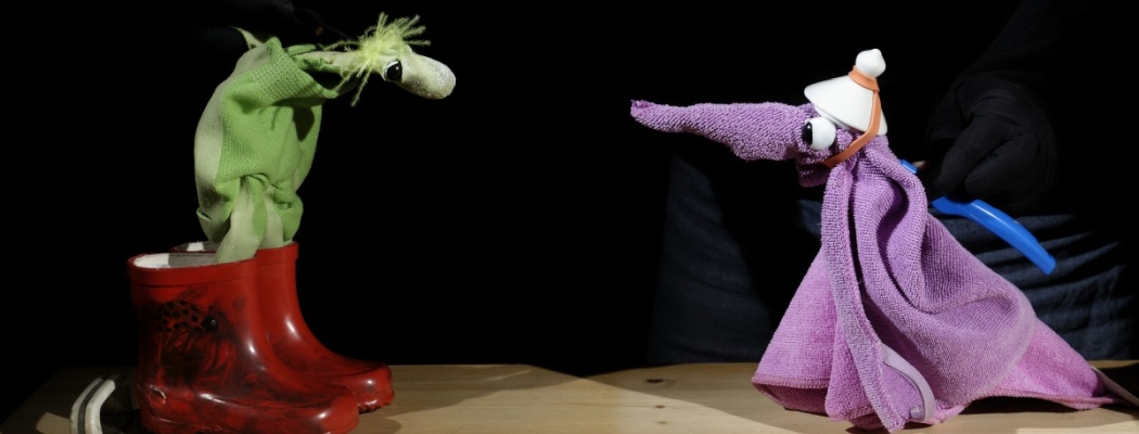 Zwei Puppenfiguren in grün und lila, die lila Figur in roten Gummistiefeln